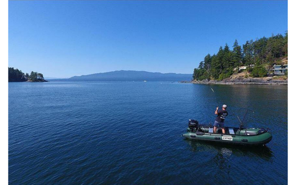 A man fishing on a lake in his inflatable boat.