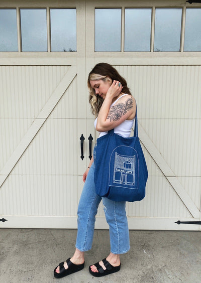 Women model holding a denim tote with a sketch of the petparknride store front on it.