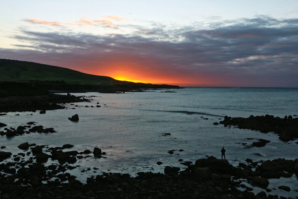 person standing on rocks surrounded by body of water overlooking sunset photo