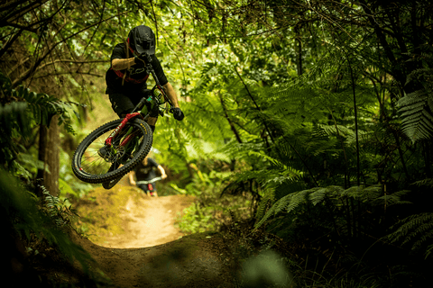 MOUNTAIN BIKER CATCHES AIR OFF A ROLLER IN THE WOODS