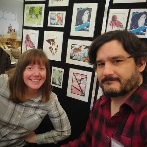 David and Jennie in front of a display of screen print artwork.