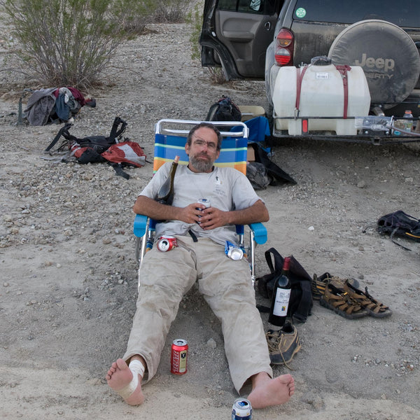 A man sitting in a lawn chair looking kid of beat up and tired, with a few empty beer cans scattered around. 