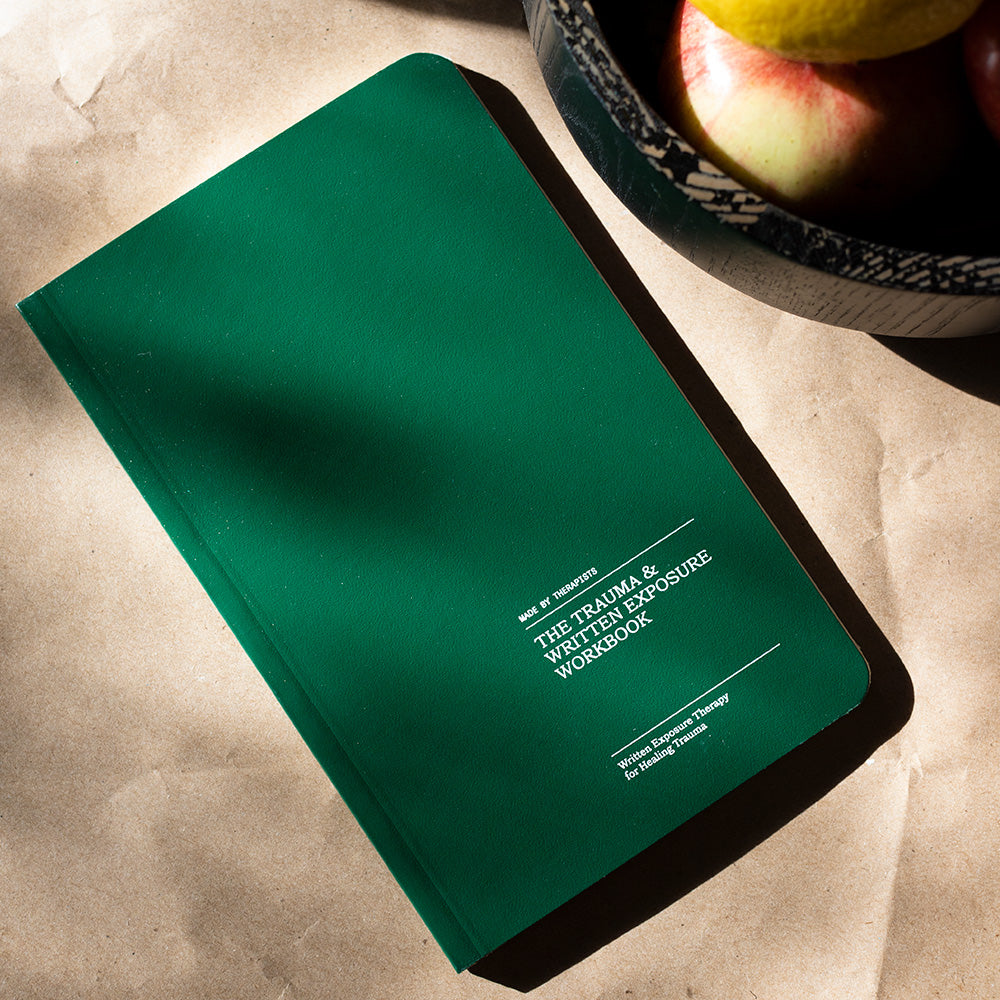Trauma & Written Exposure Workbook Therapy Notebook on a flat surface next to a bowl of fruit.