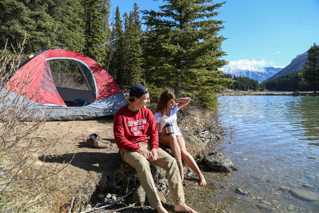 Girl and guy wearing 60°N 95°W clothing sitting by the waters edge smiling