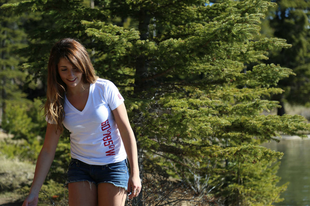 Girl wearing a 60°N 95°W white v-neck t-shirt walking along the shore