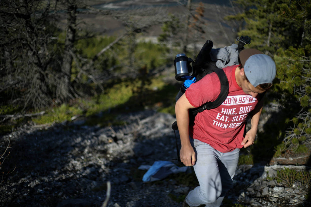 Man wearing a faded red t-shirt walking up a mountain with his camping gear on his back