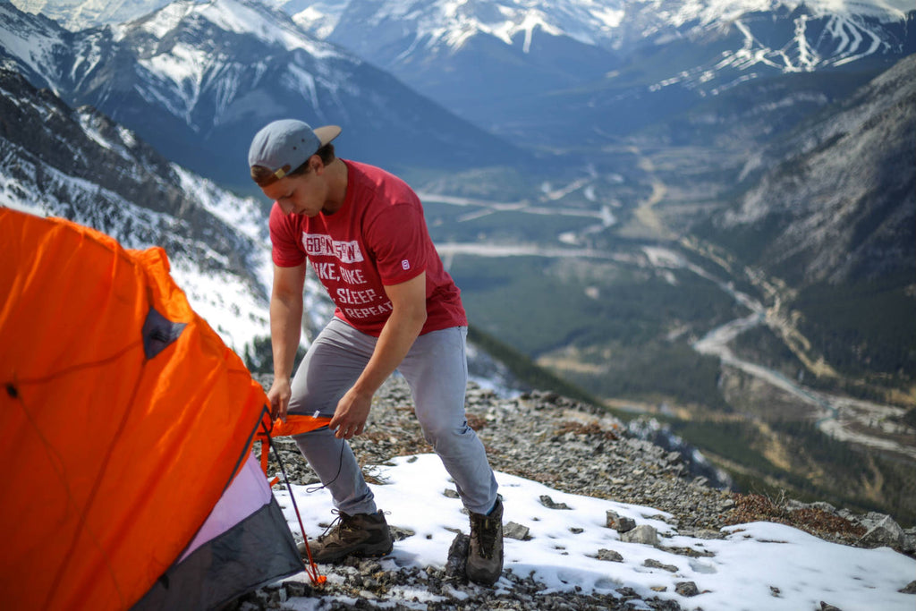 Man fastening a tent wearing a 60°N 95°W faded red t-shirt