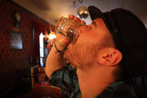 A man drinking the sourtoe cocktail club drink with the human toe touching his lips.