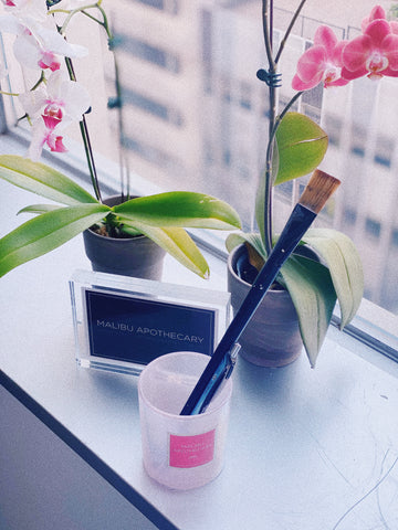 Malibu Apothecary iridescent pink scented candle jar being reused to hold pain brushes next to flowers on a shelf