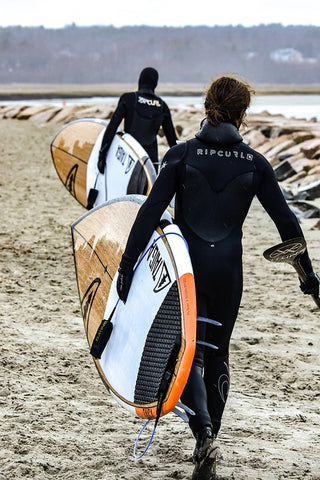 People carrying SUPs across beach