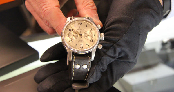 Gloved hand holding Hamilton Khaki Harrison Ford Wrist Watch silver dial with brown band and stainless steel case