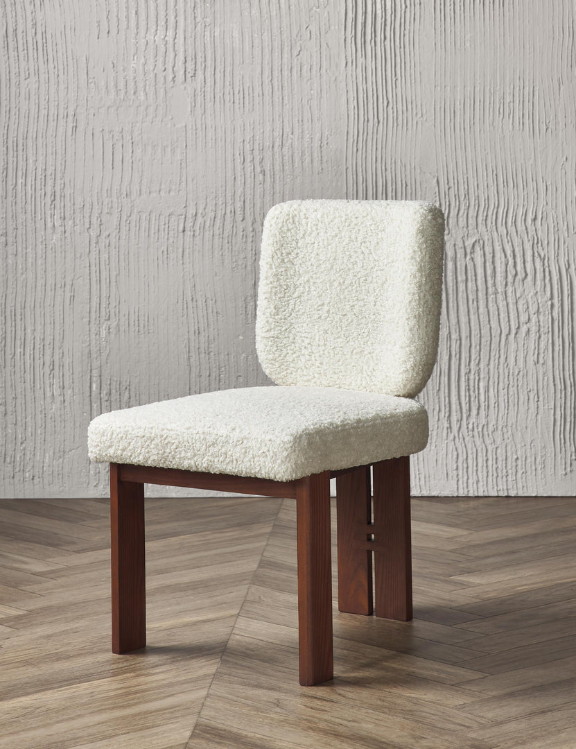 Angled view of the Sydney white plush armless dining chair sitting on chevron hardwood flooring with a texture white wall in the background.