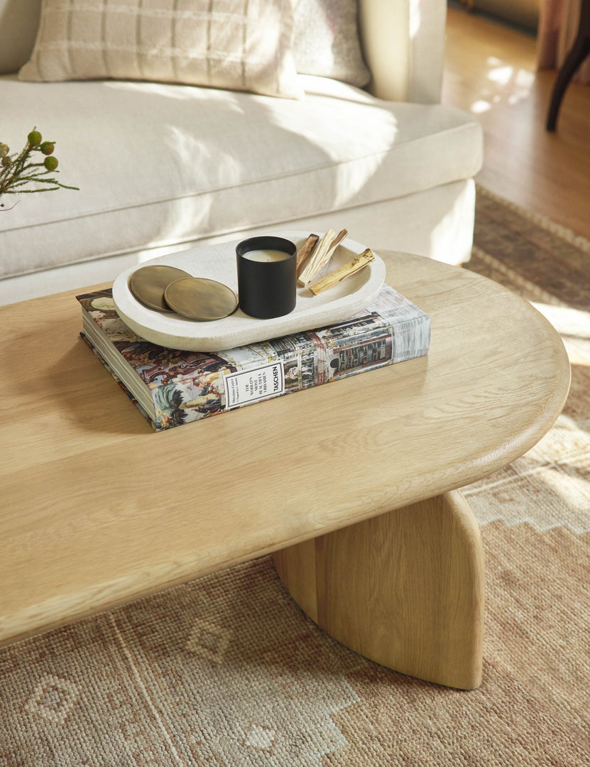 The Ada solid oak oval coffee table sits in front of an ivory couch in a living room with a neutral geometric area rug.