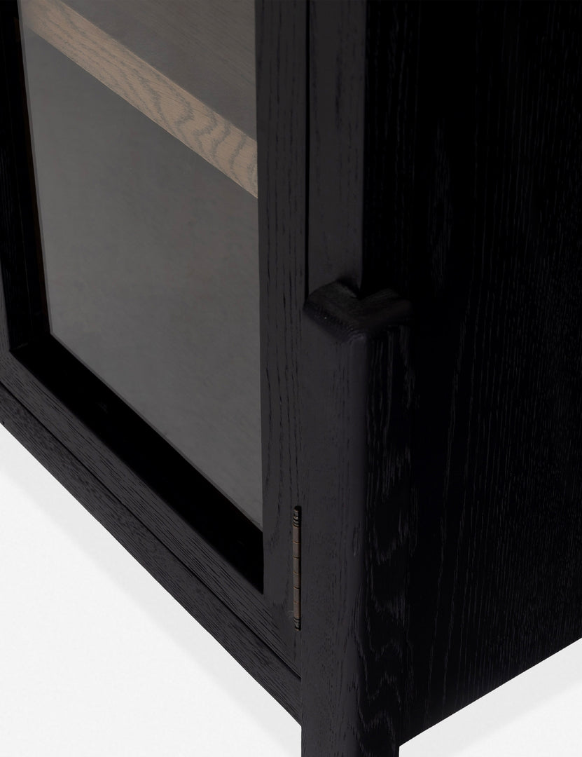 Close-up of the corner edge of the Apolline black wooden arched curio cabinet with gold door handles
