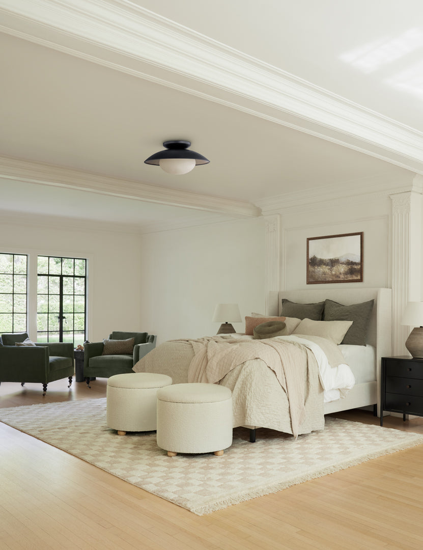 The Adara talc linen upholstered bed sits in a large bedroom atop a checkerboard rug to the right of a sitting nook featuring two green velvet accent chairs.