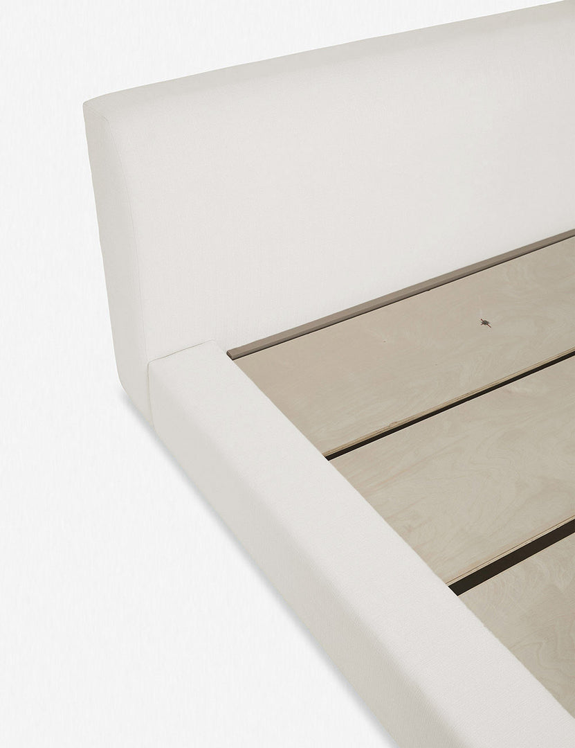 Close-up of the left side of the Clayton ivory upholstered platform bed featuring the headboard, side paneling, and wooden support beams