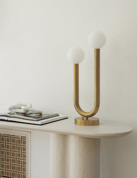 #color::natural-brass | The Happy gold, natural brass table lamp by Regina Andrew with a dual-metal tube silhouette with contrasting matte white bumbs sits on a white sideboard next to marble decor and a stack of open books