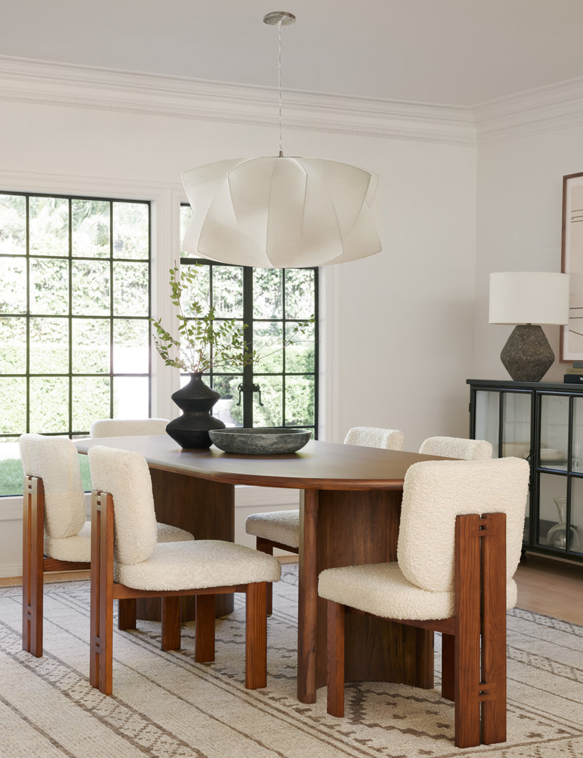 The Sydney white plush armless dining chair sits in a dining room surrounding an oval wooden dining table underneath a white sculptural chandelier.
