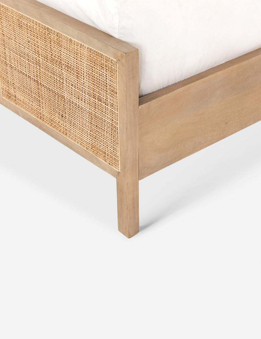 Close-up angled side view of the light wood base and cane detailing on the Hannah bed.