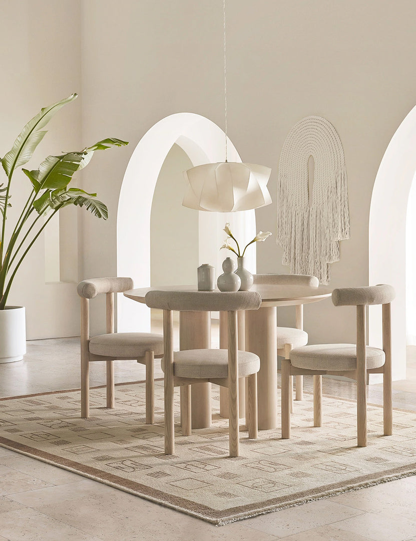 The Mojave white round dining table with an architectural base sits in a white monochrome dining room surrounded by four rounded dining tables underneath a white sculptural chandelier.