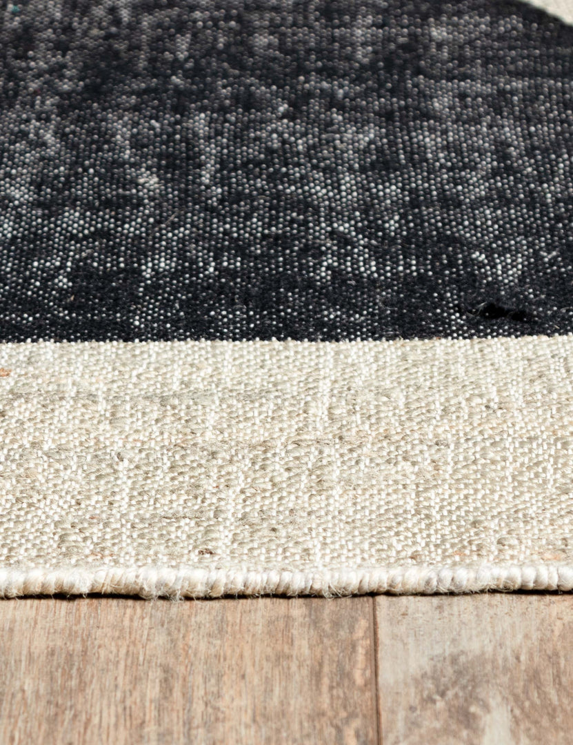 Close-up of the black semi-circle and neutral toned fabric on the Goubi flatweave area Rug by Lemieux et Cie x Momeni