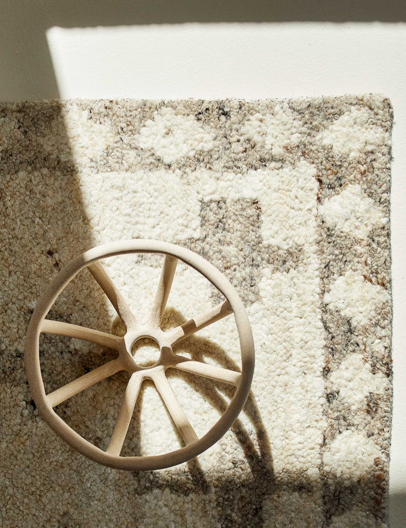 A neutral ceramic open bowl lays on a corner of the Acoma cream and tan plus-sign patterned Moroccan area rug with diamond border.