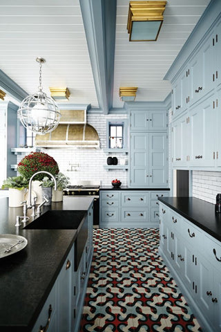 Farmhouse blue kitchen cabinets with copper pulls black countertop and a blue mosaic floor