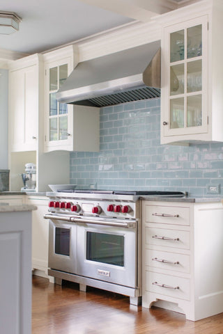Glossy blue backsplash paired with a industrial stovetop and traditional white cabinets and contemporary cabinet hardware