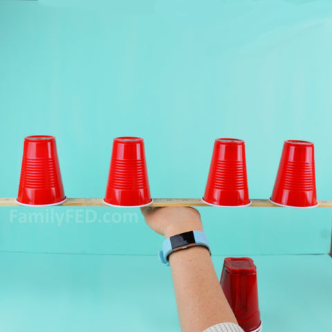 Balance the yardstick and cups on the back of your hand.