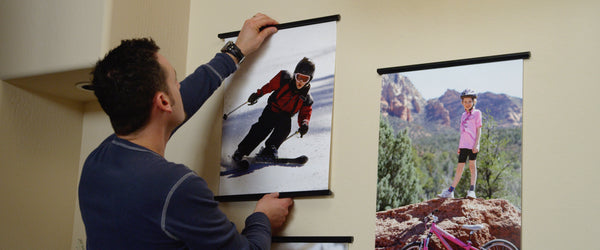 father hanging a poster of daughter skiing on a wall using a posterhanger 