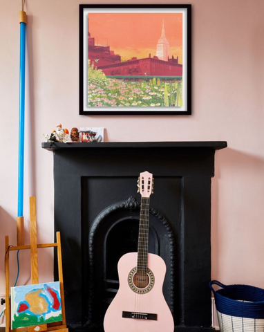 pink wall with bold artwork framed above a black victorian fireplace