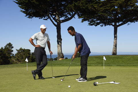 Tiger Woods and student putting on golf hole together.