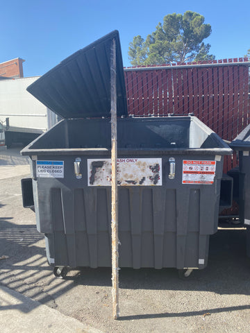 dumpster with lid propped open using wood pole