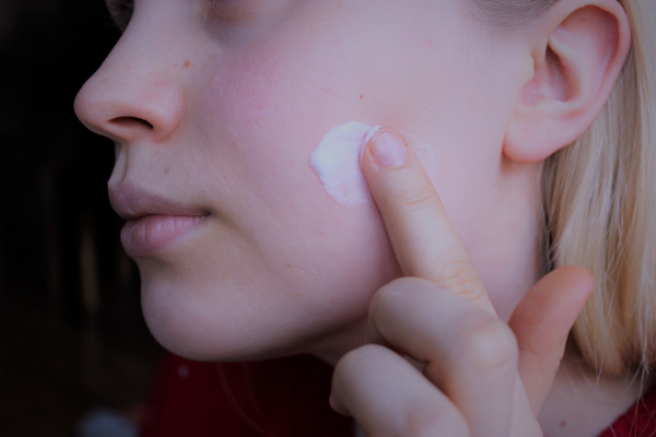 woman putting cream on left check with her left index finger