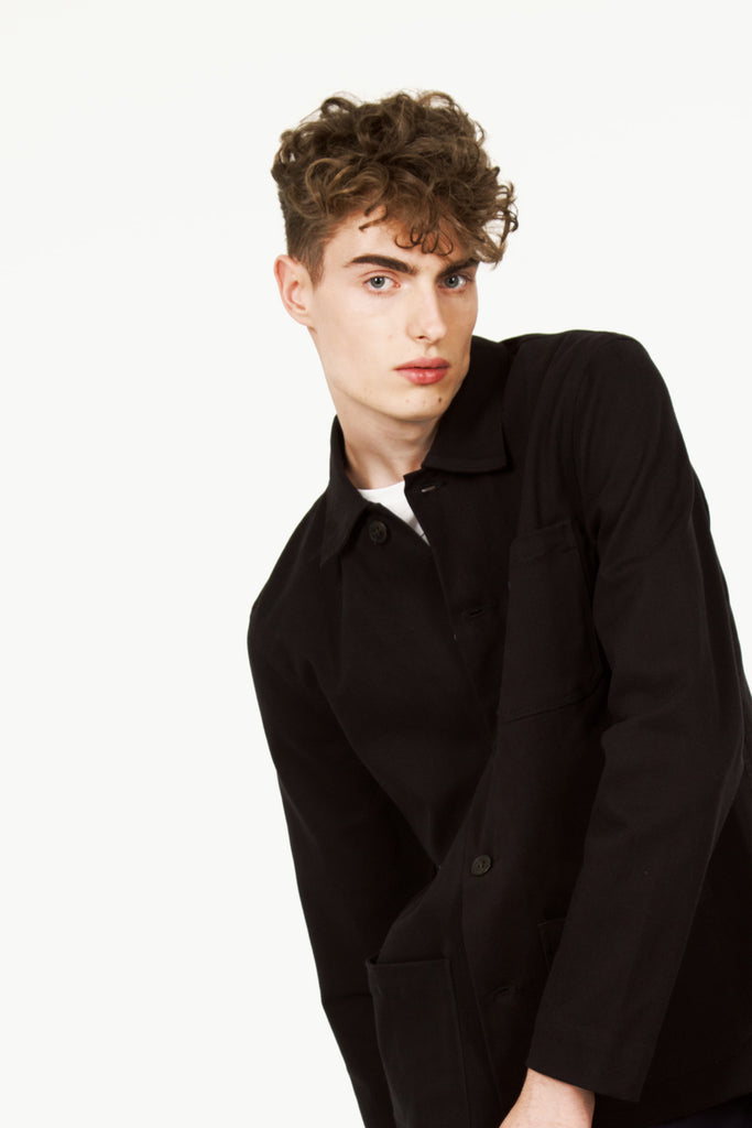 Jeune homme hipster parisien porte une veste de travail minimaliste pour homme noire coupe droite 