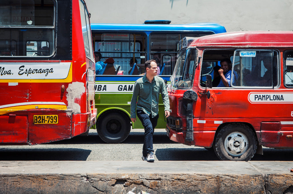 Aurelyen traversant une rue de Lima, dans le chaos de la circulation, bus et voitures colorés, ambiance latino