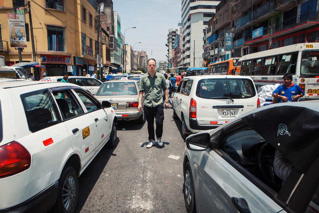 Aurelyen traversant une rue de Lima, dans le chaos de la circulation, bus et voitures colorés, ambiance latino