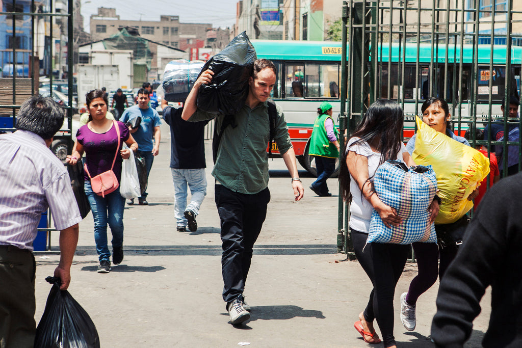 Homme marchant dans la foule de Lima, tient sur ses épaules un sac remplis de tissus pour développer une collection prêt-à-porter