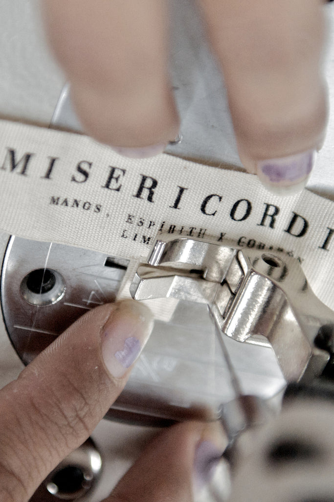  Travail artisanal détail d'une main en train de coudre une étiquette en coton sur un vêtement