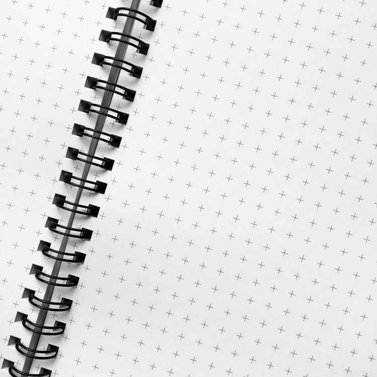 A spiral notebook open flat showing grid graph pages and the black spiral wire.
