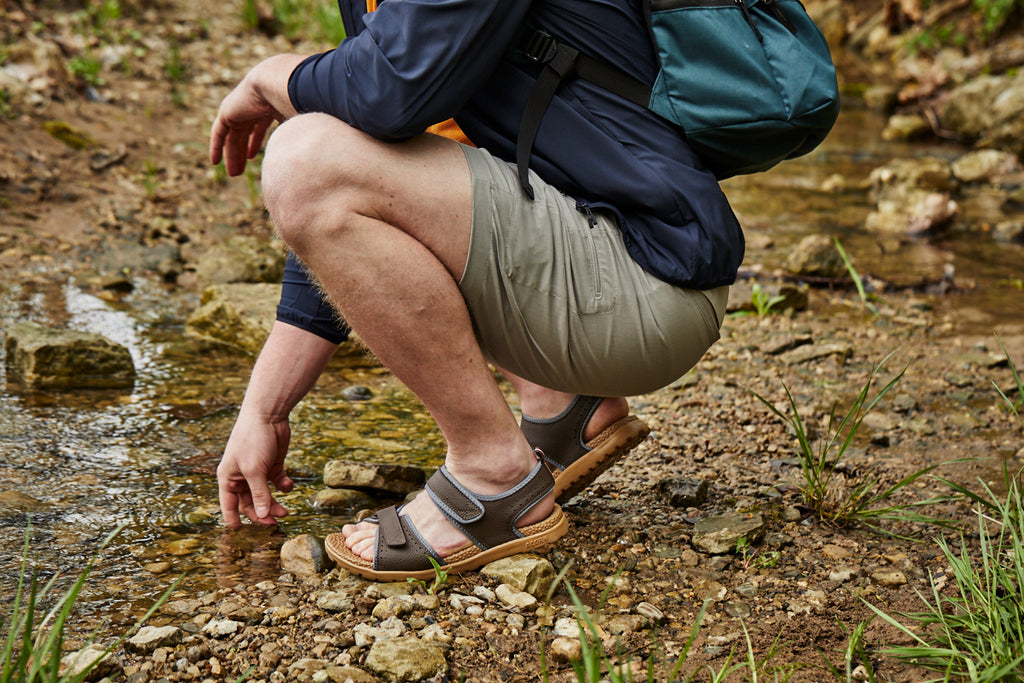 Men's Grafton Sandal in Navy on Model picking up a rock in a creek