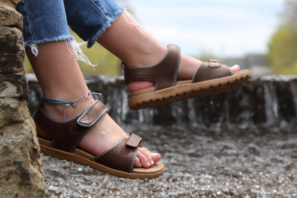 Woman wearing Grafton Everywear Sandal in walnut sitting on the side of a small waterfall