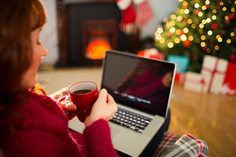 Redhead holding hot drink and using laptop at christmas in the living room