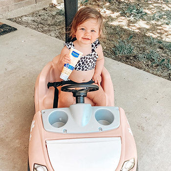 baby driving around in toy car holding Mustela baby products