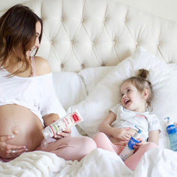 Pregnant mom and daughter on bed laughing