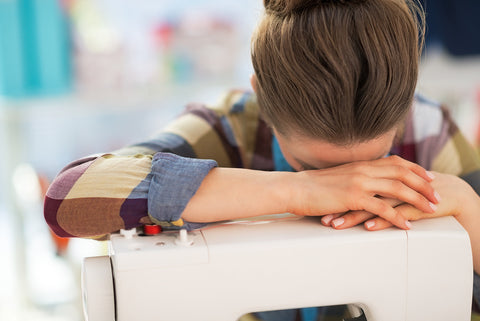 A stressed-out seamstress leaning her head over her sewing machine.