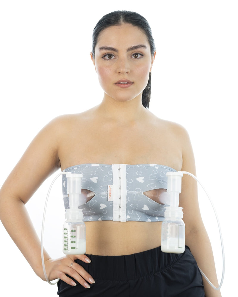 A person stands facing the camera with their hand on their hip. They are wearing a PumpEase hands-free pumping bra in a grey and white Xs and Os print.