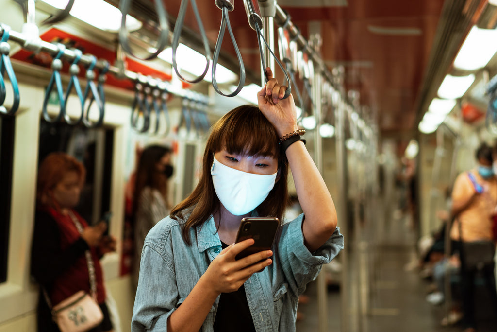A woman wearing a face mask in a subway while using her phone