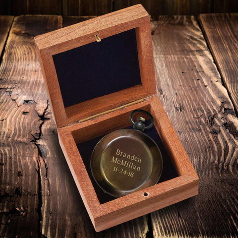 A bronze colored compass sitting in a brown wooden box