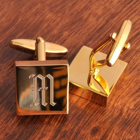 Two high-brass polished cufflinks sitting on a brown table with the letter M in the middle